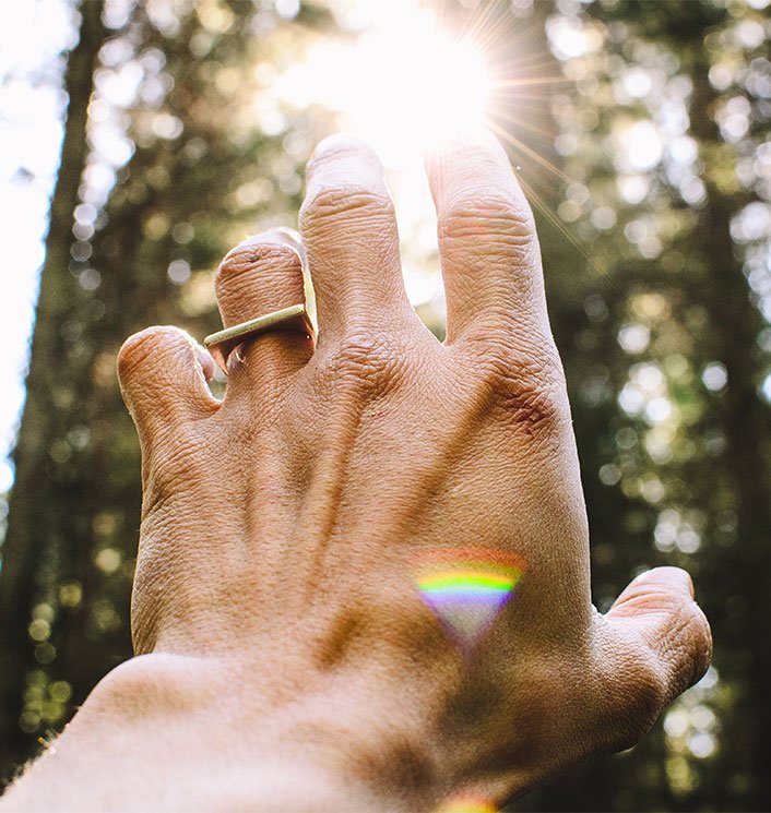 hand reaching out to sun with chakra colors on the back